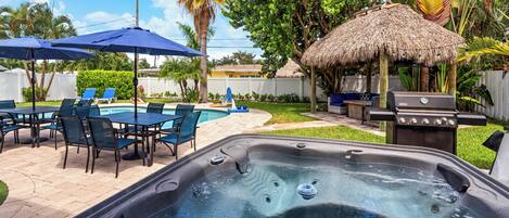 A backyard with a hot tub, outdoor seating, a barbecue grill, and a pool.