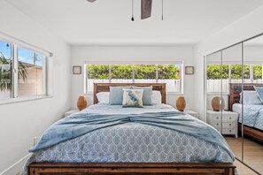 Ein Schlafzimmer mit einem großen Bett, einem Holz-Kopfteil, einem Fenster mit Blick auf Grünflächen und einem Spiegel an der Wand.