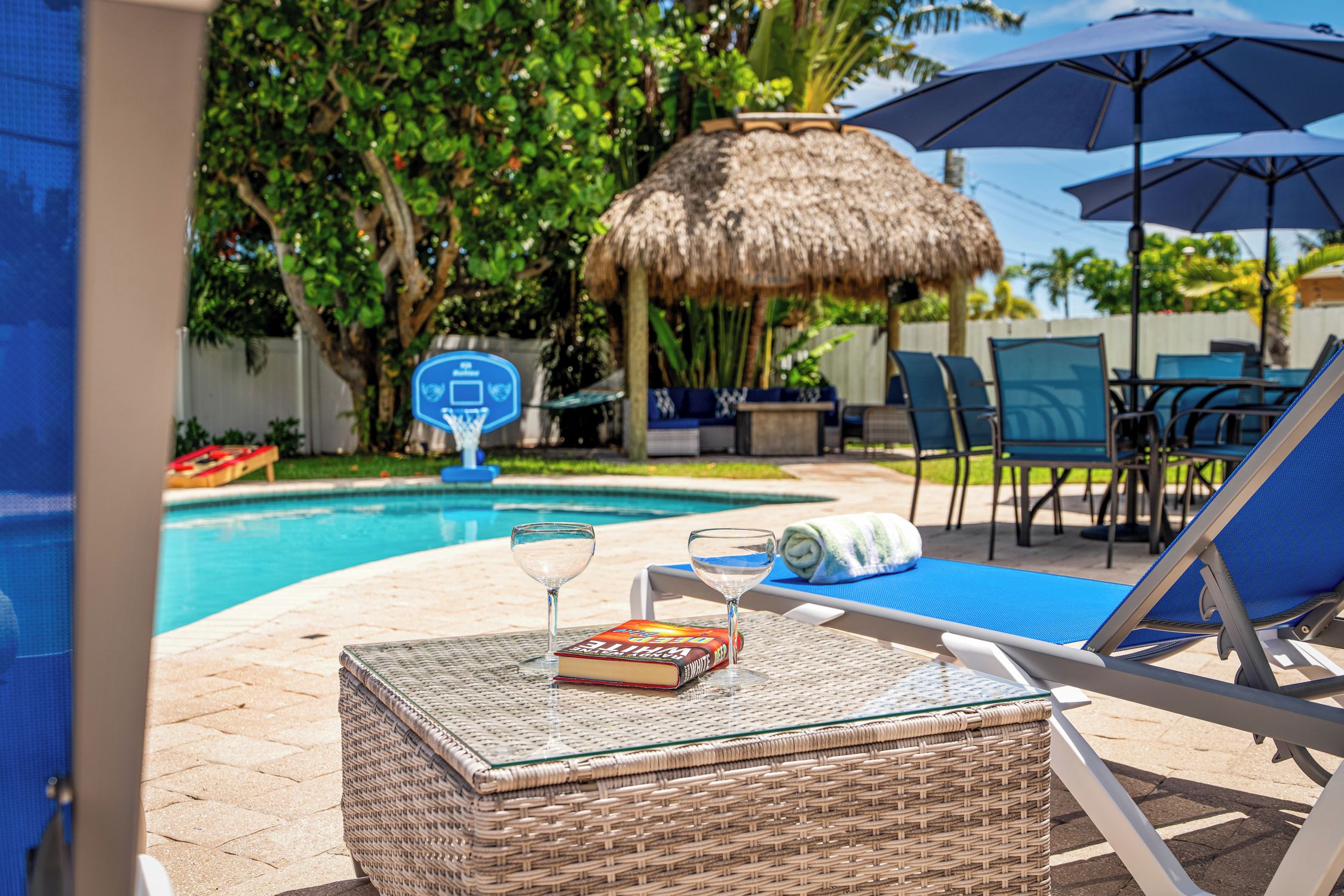 A poolside area with a lounge chair, a table with a book and a glass, and a thatched umbrella.