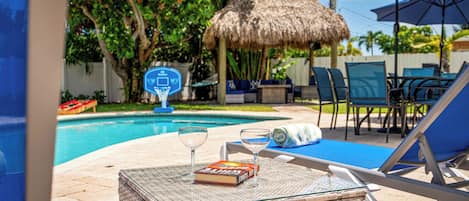 A poolside area with a lounge chair, a table with a book and a glass, and a thatched umbrella.