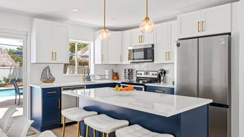 A modern kitchen with white cabinets, a stainless steel refrigerator, and a central island with bar stools.