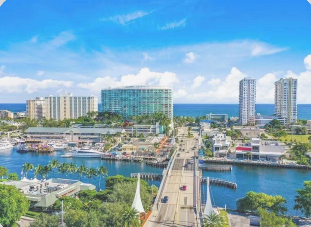 A coastal cityscape with a marina, high-rise buildings, and a clear blue sky.