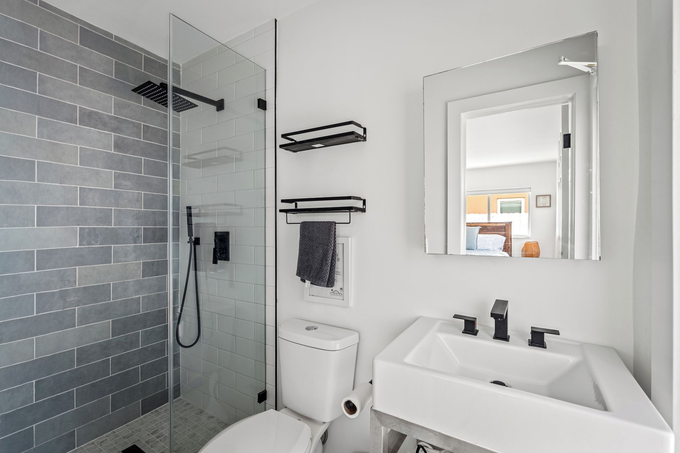 A modern bathroom with a glass shower enclosure, a white toilet, a white sink, and a mirror above the sink.