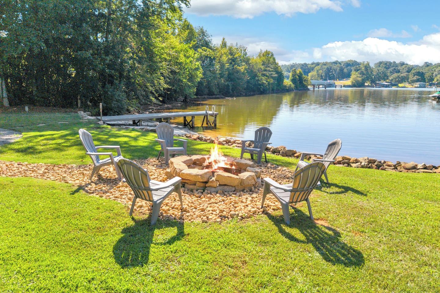 Een terras aan het meer met een vuurkuil en Adirondack stoelen.