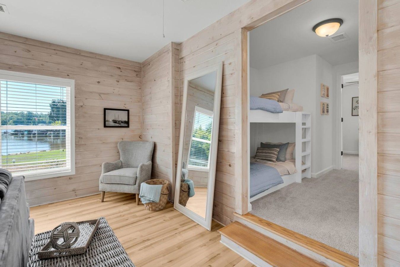 A cozy room with a wooden floor, a grey armchair, a small table, and a bunk bed.