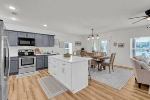 Une cuisine moderne avec des meubles gris, un îlot central blanc et un coin repas comprenant des chaises et une table en bois.