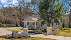 A single-story house with a front porch, a paved driveway, and a landscaped front yard with a stone wall and a tree. - The Eddie At Mount Carmel- Peaceful, Sleeps 4 (Monroe)