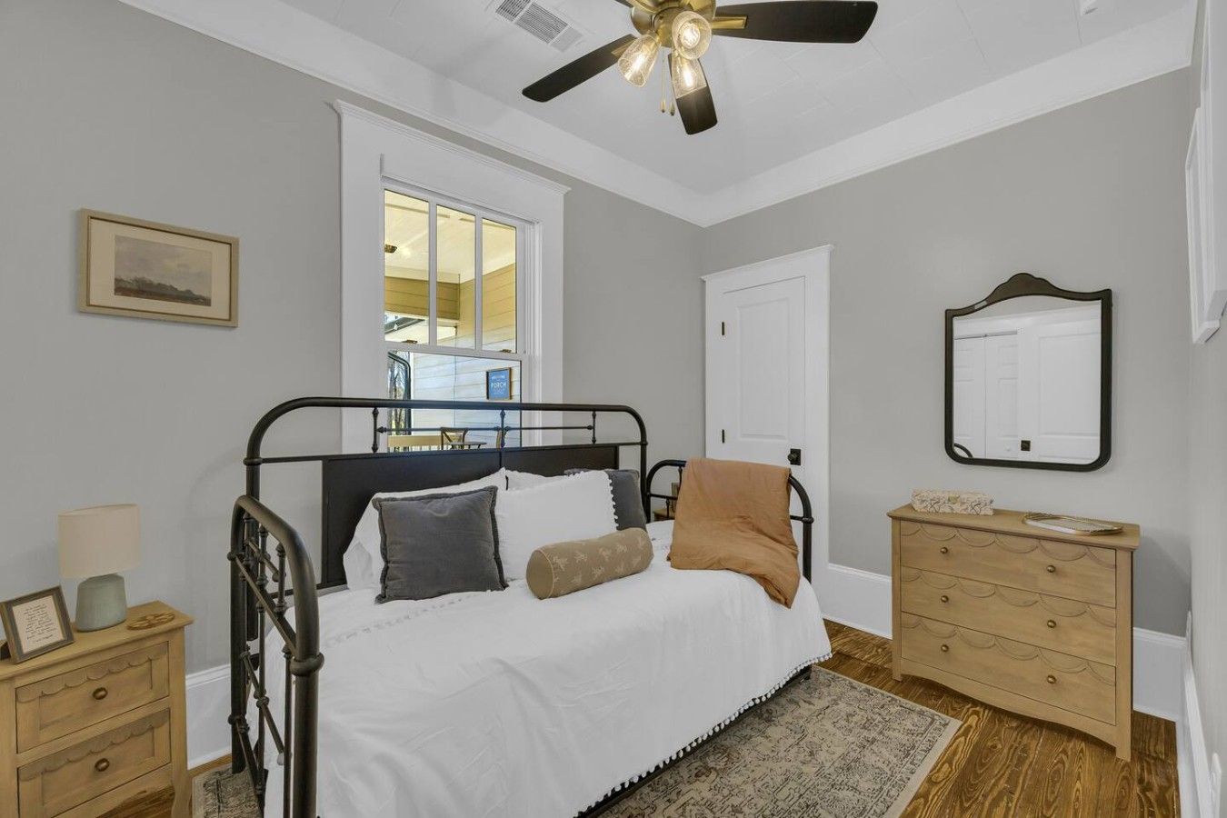A bedroom with a bed, bedside tables, a dresser, a ceiling fan, a window, and a door.