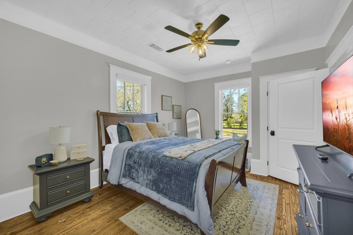 A bedroom with a bed, dresser, nightstand, lamp, ceiling fan, and a TV.