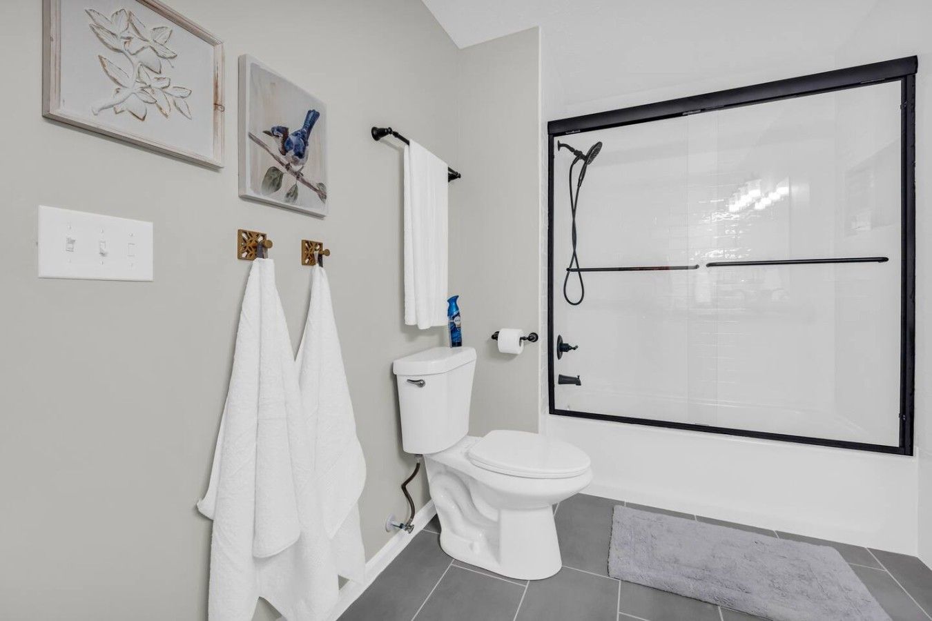 Un baño moderno con inodoro, cabina de ducha y dos toallas colgadas en ganchos.