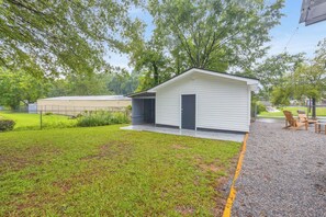 A small, single-story building with a door and a window, surrounded by a grassy area and trees.