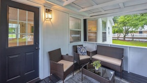 A covered porch with wicker furniture, a glass table, and a door with a window.