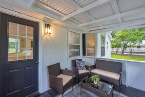 A covered porch with wicker furniture, a glass table, and a door with a window.