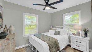 A bedroom with a bed, bedside tables, a nightstand, a ceiling fan, and windows with blinds.
