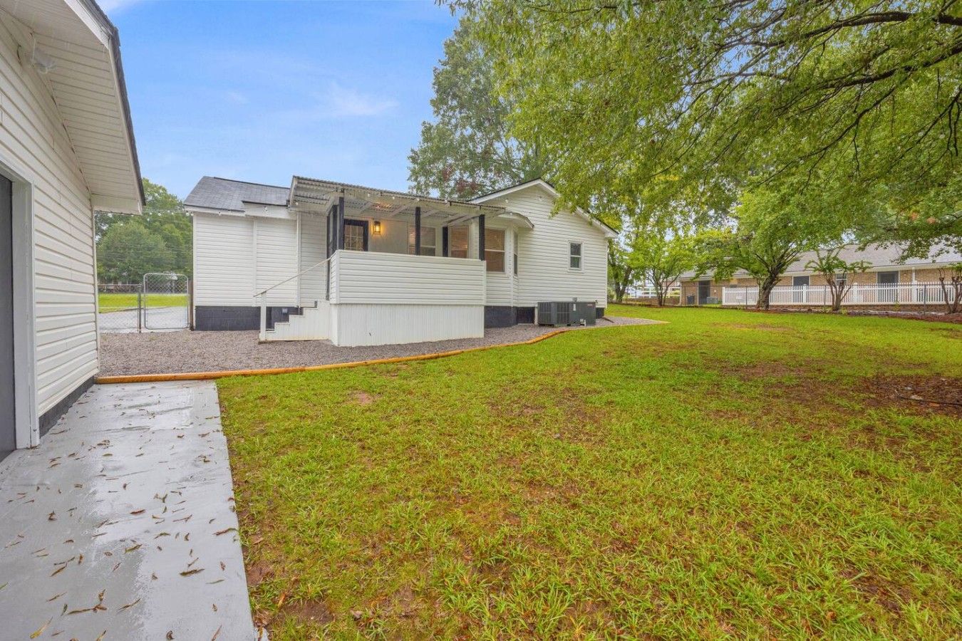 A single-story mobile home with a covered porch, a small front yard, and a tree to the right.