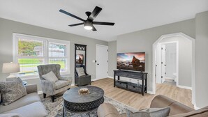A living room with a ceiling fan, a flat-screen TV, a round coffee table, and a sofa.