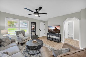 A living room with a ceiling fan, a flat-screen TV, a round coffee table, and a sofa.