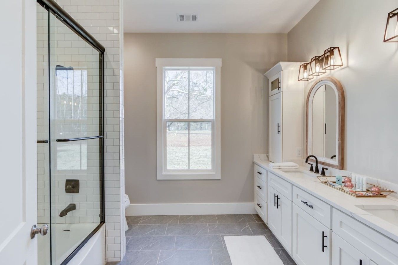 A modern bathroom with a glass shower enclosure, a large window, and a vanity with a mirror.