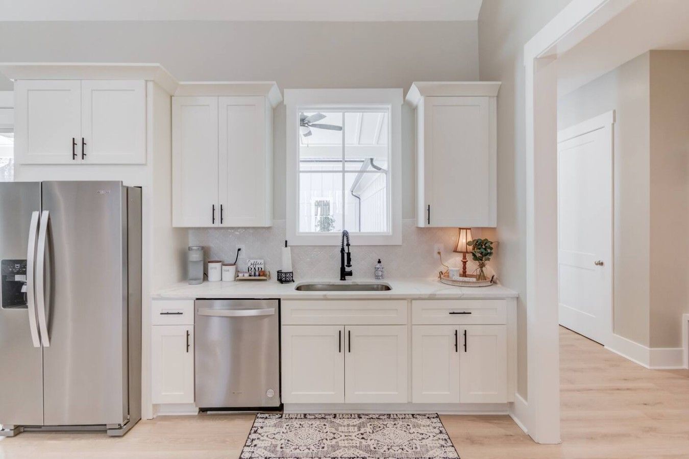 Una cocina moderna con armarios blancos, un refrigerador de acero inoxidable, un lavavajillas y un ventanal sobre el fregadero.