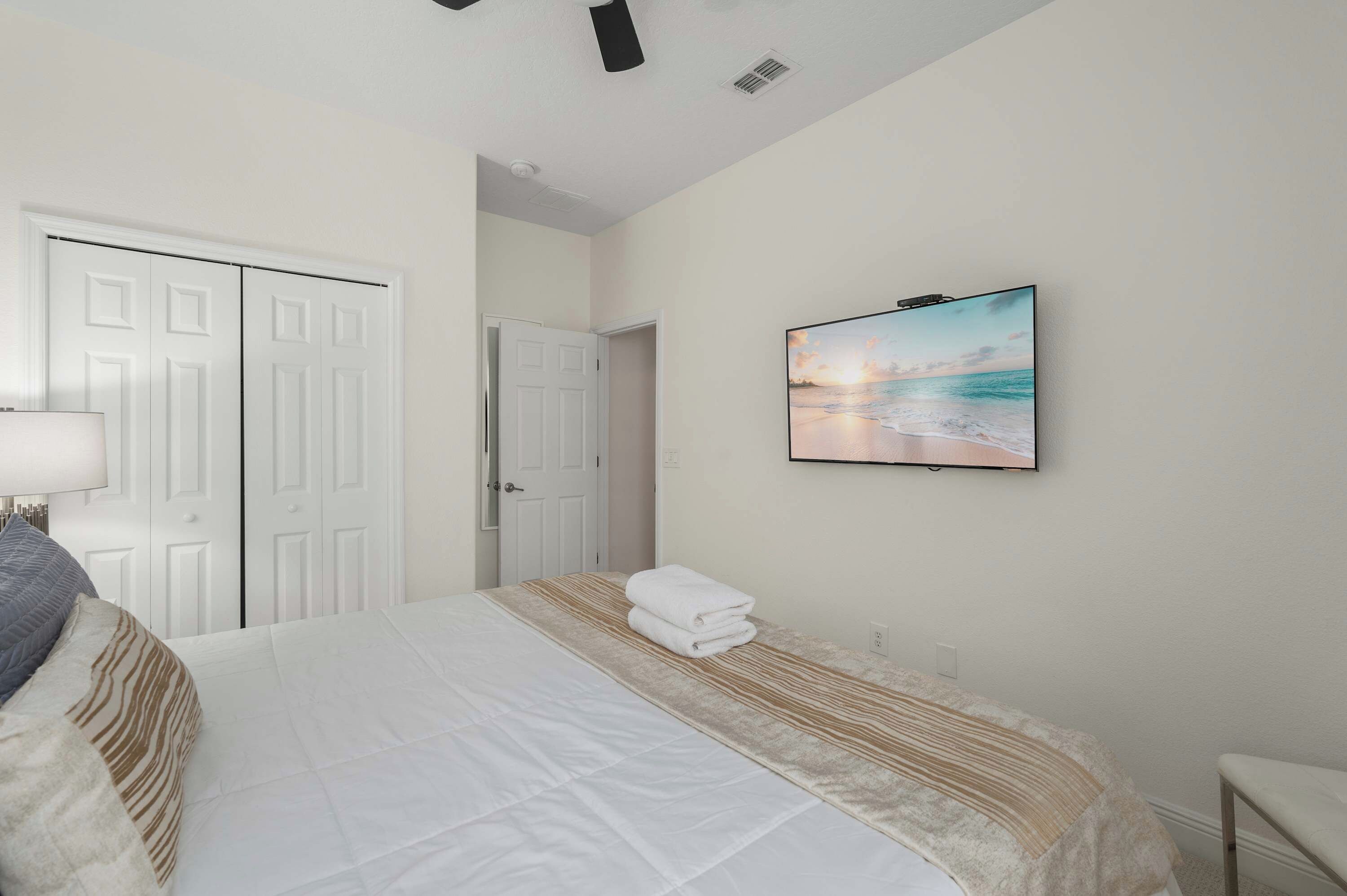 A bedroom with a bed, a wall-mounted TV, a door, and a window.
