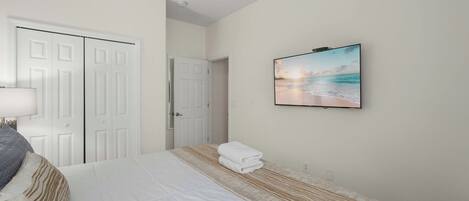A bedroom with a bed, a wall-mounted TV, a door, and a window.