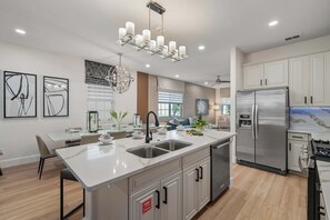 A modern kitchen with a central island, stainless steel appliances, and a dining area with a glass table. - 4BR Near Disney - Private Heated Pool & Spa (Kissimmee)