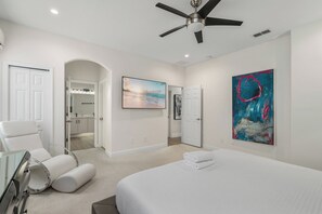 A modern bedroom with a bed, a ceiling fan, a bathroom with a vanity, and a large abstract painting. - 4BR Near Disney - Private Heated Pool & Spa (Kissimmee)