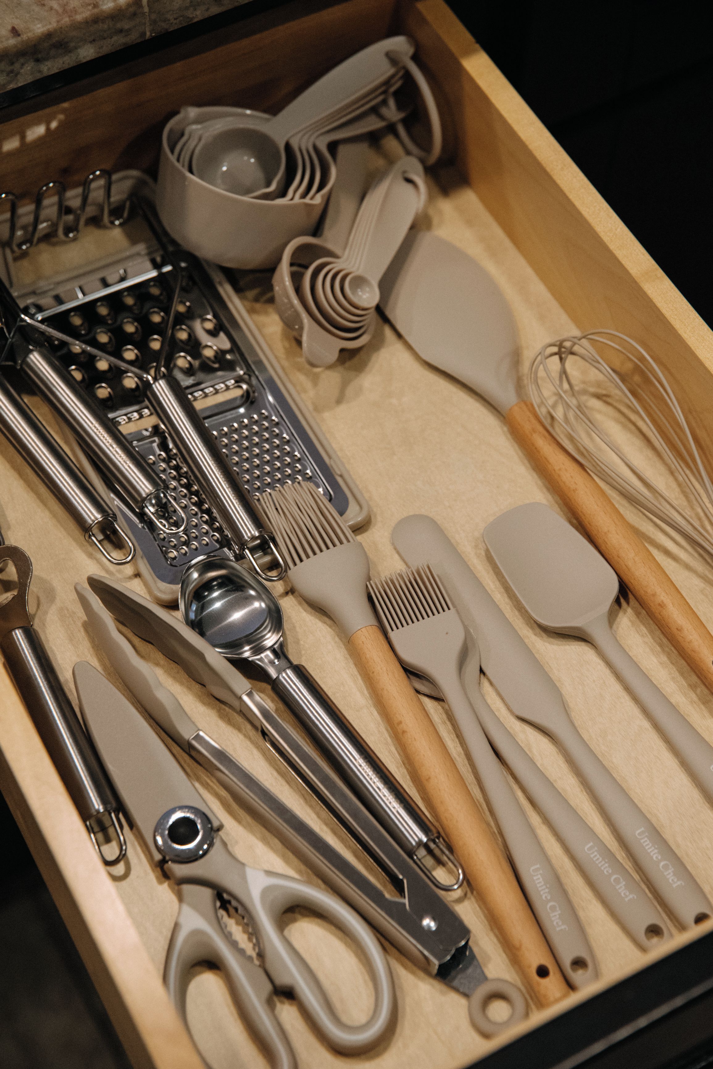 A drawer containing various kitchen utensils including a grater, spatulas, a whisk, and a pair of scissors.