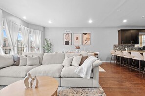 A modern living room with a sectional sofa, a dining area with a table set for four, and a kitchen with dark cabinetry. - Elegant & Cozy MetLife NYC /2 FREE Parking / Gameroom (Jersey City)