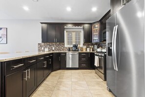A modern kitchen with dark cabinetry, stainless steel appliances, and a tiled backsplash. - Elegant & Cozy MetLife NYC /2 FREE Parking / Gameroom (Jersey City)