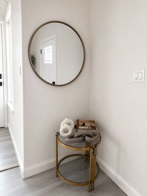 A hallway with a round mirror on the wall, a small round table with decorative items, and a door with a window. - Modern Luxe Retreat – 3BR/2BA Home Near Med Center, NRG, & Downtown Houston (Houston)