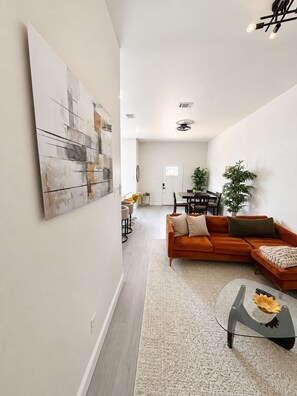 Ein modernes Wohnzimmer mit einem Ecksofa, einem Glastisch und einem Essbereich im Hintergrund.