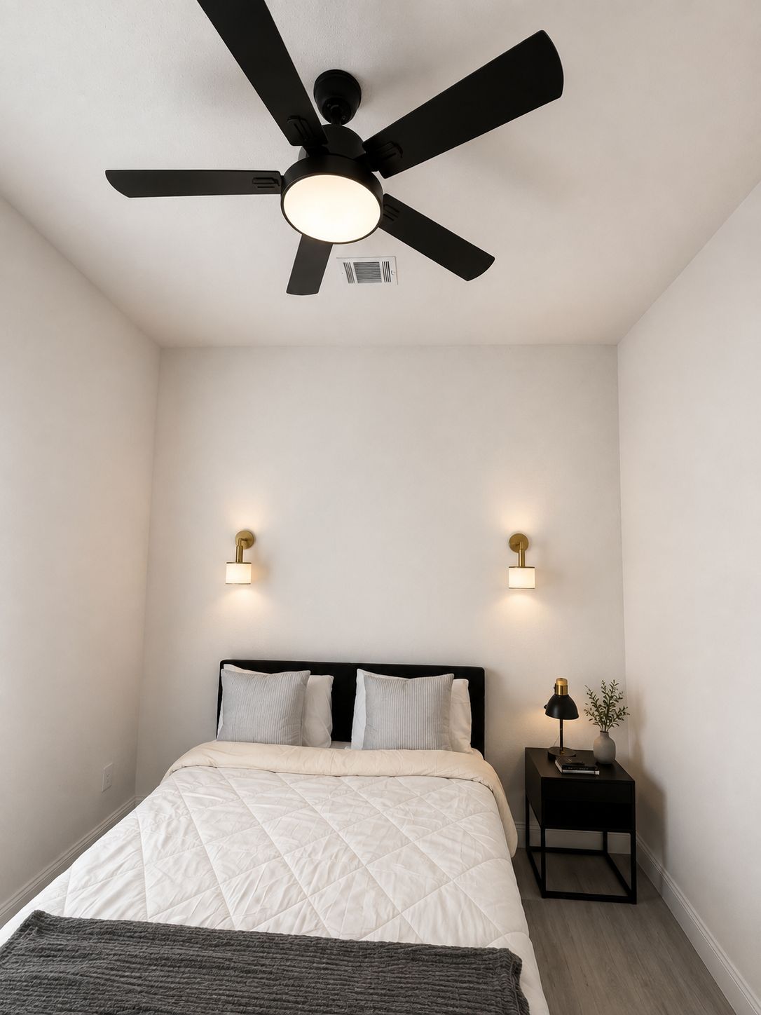 Une chambre à coucher comprenant un lit, un ventilateur de plafond, deux lampes fixées au mur et une table de chevet avec une lampe.