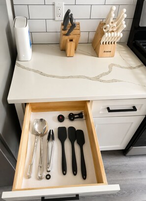 A kitchen counter with a marble top, a knife block, and a drawer with kitchen utensils. - Modern Luxe Retreat – 3BR/2BA Home Near Med Center, NRG, & Downtown Houston (Houston)