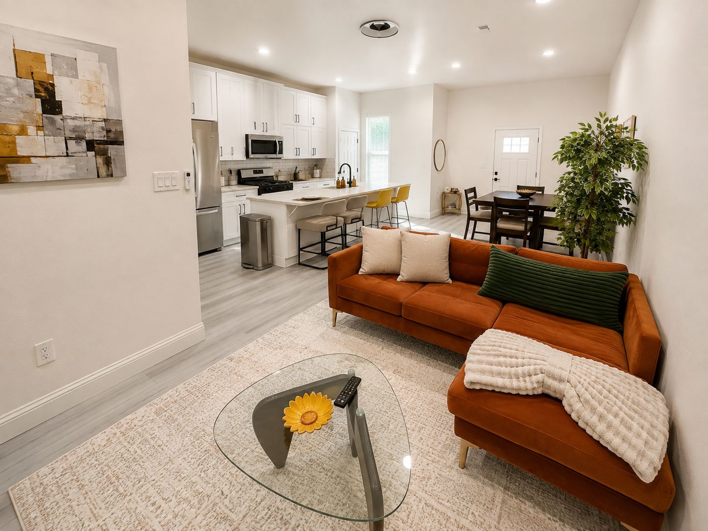 A modern living room with a sofa, a coffee table, and a dining area in the background.