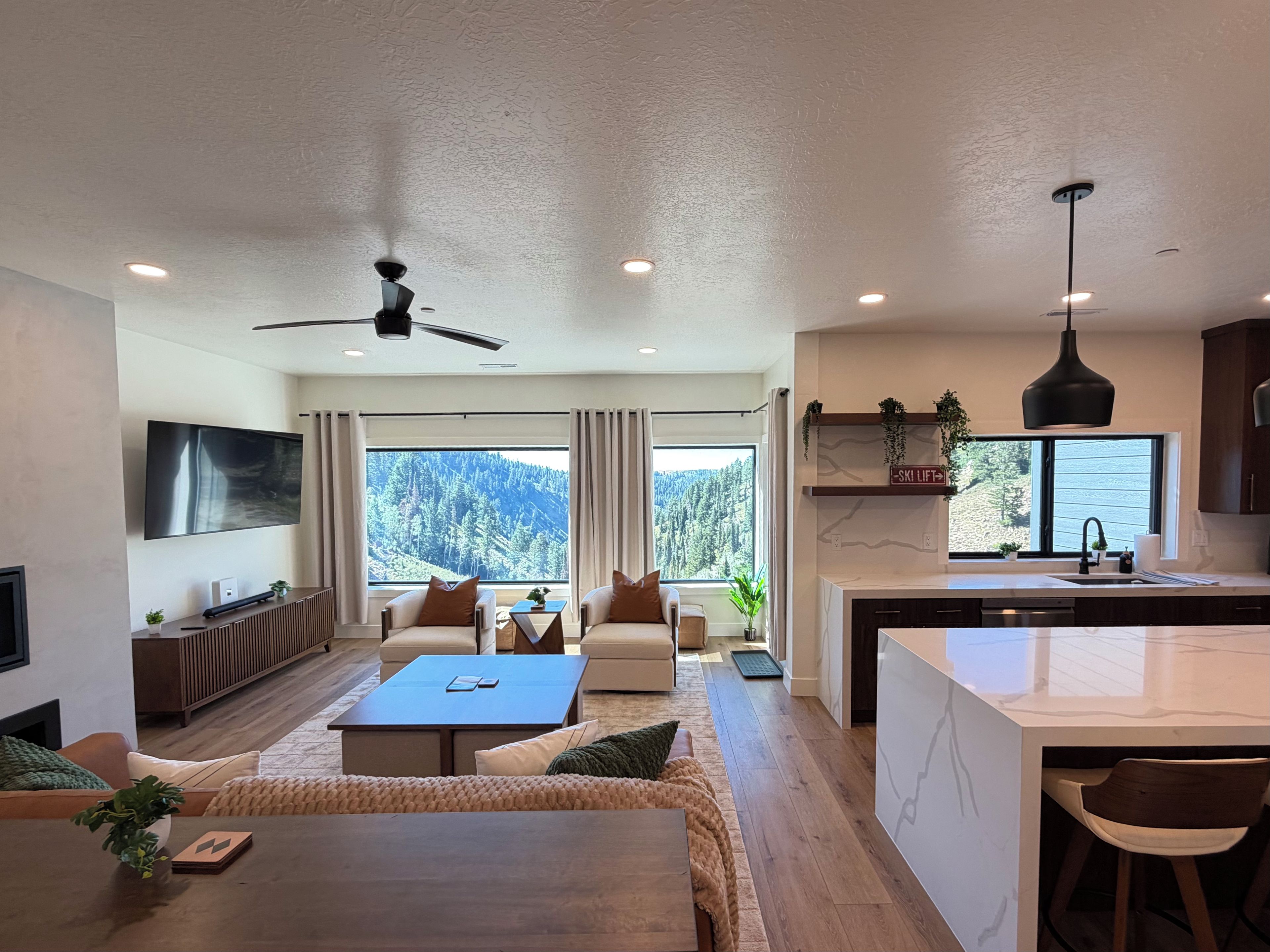 A modern living room with a sofa, coffee table, and a TV. There is a kitchen area with a dining table and chairs.