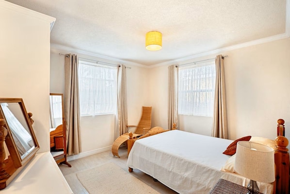 A hotel room with a bed, a chair, a lamp, and a window with curtains. - Barbados dream home - the perfect place to stay (Oistins)