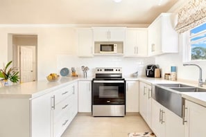 A modern kitchen with white cabinetry, stainless steel appliances, and a large window providing natural light. - Barbados dream home - the perfect place to stay (Oistins)