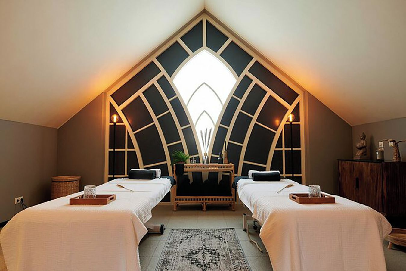 A room with two beds, a central table, and a unique arched ceiling design.