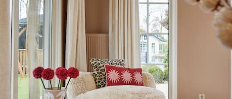 Una habitación con un ventanal grande, un sofá blanco mullido y un jarrón con flores rojas.