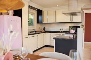A modern kitchen with a central island, a pink refrigerator, and a dining area with a table set for two. - 8P Veluwe Wellness Villa | Sauna, Hot Tub & BBQ (Voorthuizen)