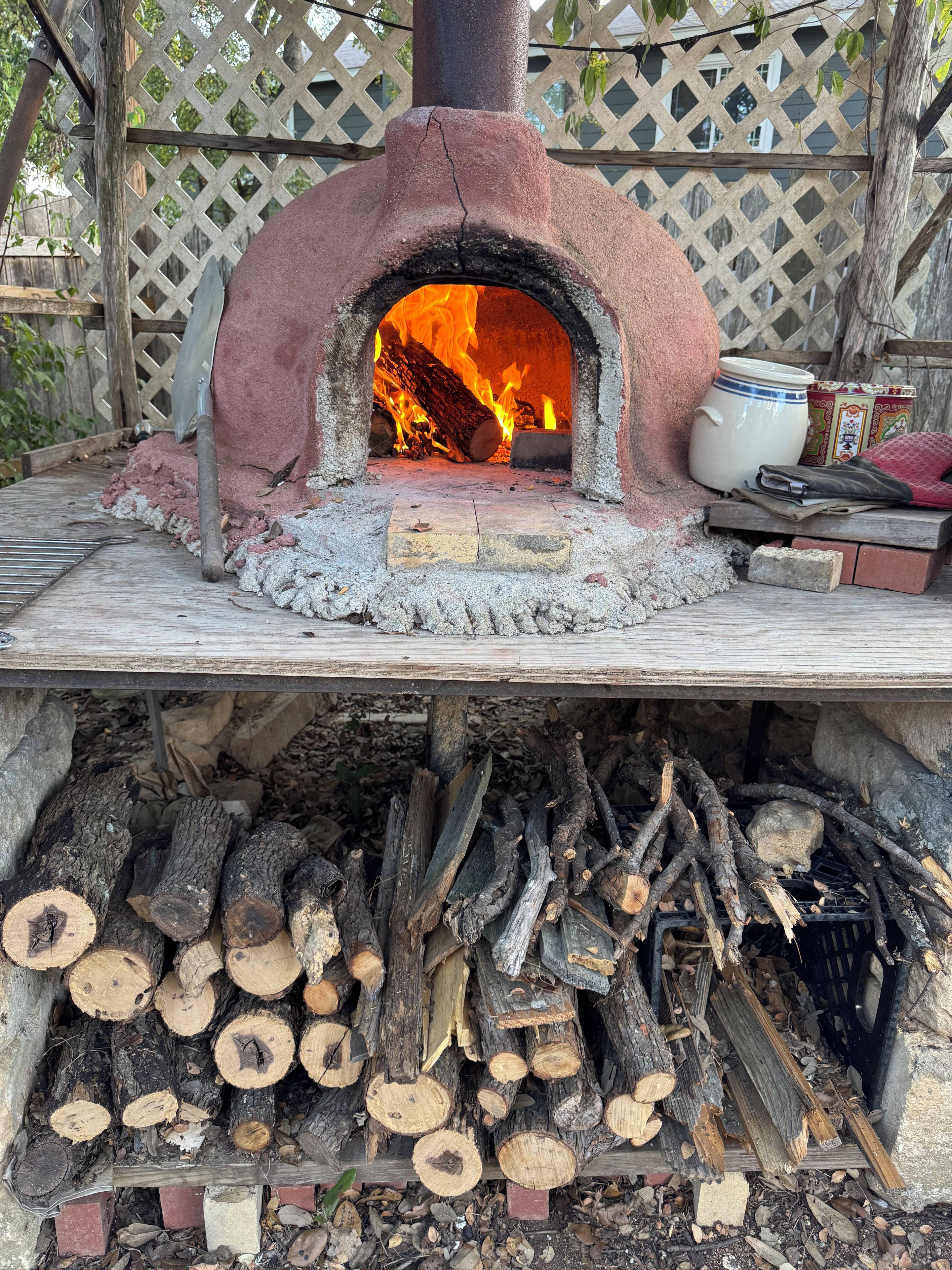Un horno de pizza a leña con fuego encendido, rodeado de leños y ladrillos.