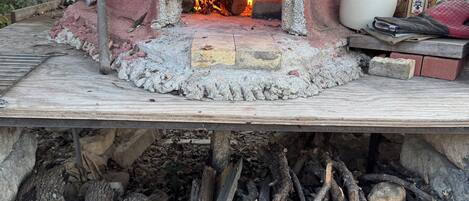 Un horno de pizza a leña con fuego encendido, rodeado de leños y ladrillos.
