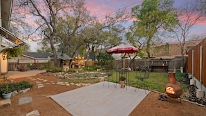 Ein Garten mit Terrasse, Sitzgelegenheiten im Freien, einem Feuerkorb und einem Zierzaun.