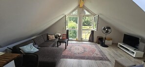 A loft-style room with a large window, a sofa, a TV, and a fan. - Gleenbach Vacation Home with a Balcony (Kirtorf)