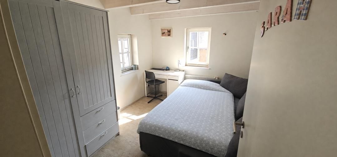 Um quarto com cama, escrivaninha e guarda-roupa.
