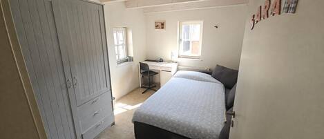 Um quarto com cama, escrivaninha e guarda-roupa.