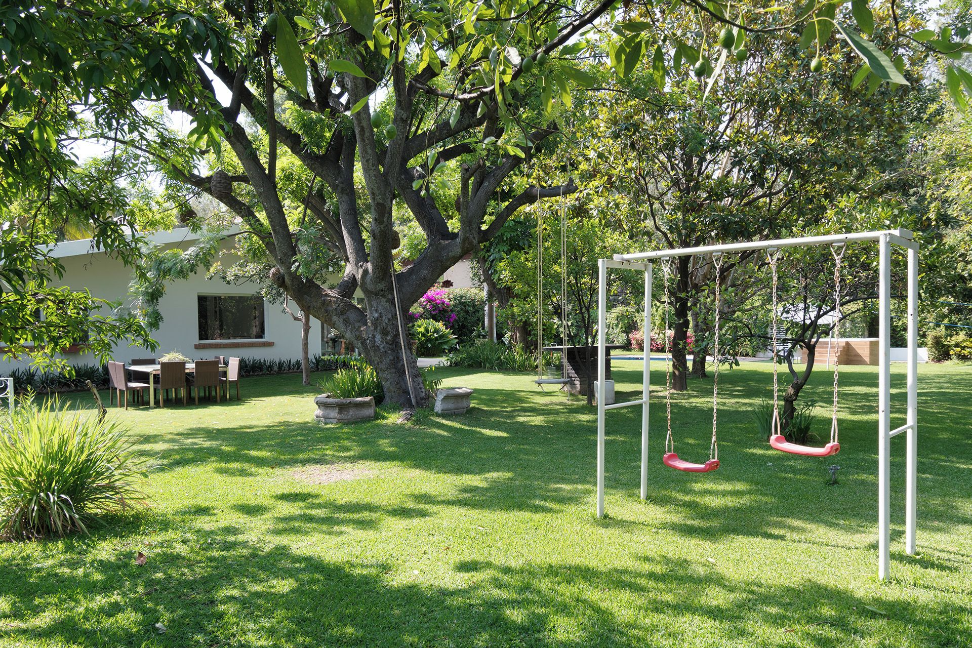 A garden with a swing set, a dining area, and a large tree.