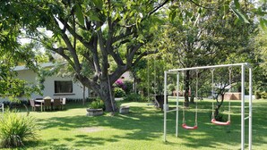 Un jardín con un columpio, una zona de comedor y un gran árbol.