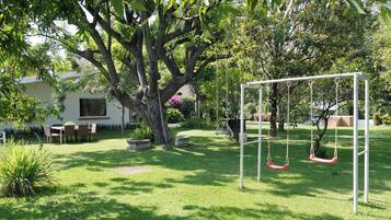 A garden with a swing set, a dining area, and a large tree.